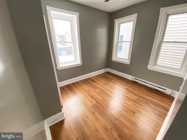spare room with a baseboard radiator, baseboards, light wood-style flooring, and a ceiling fan