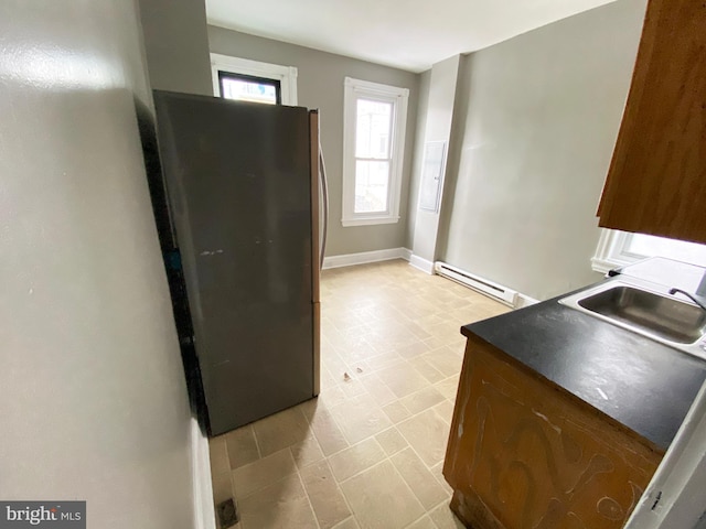 kitchen featuring freestanding refrigerator, baseboard heating, a sink, baseboards, and dark countertops