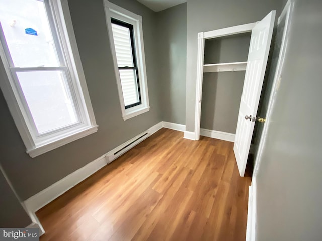 unfurnished bedroom with a baseboard heating unit, light wood finished floors, baseboards, and a closet