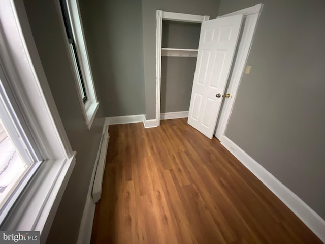 unfurnished bedroom featuring baseboards, dark wood finished floors, a closet, and a baseboard heating unit