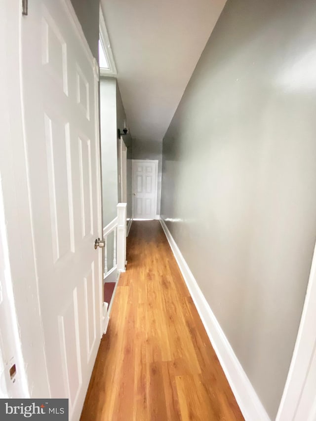 hall featuring light wood finished floors, baseboards, and an upstairs landing