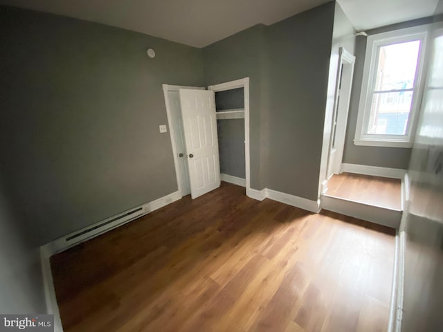 unfurnished bedroom with wood finished floors, a baseboard radiator, a closet, and baseboards