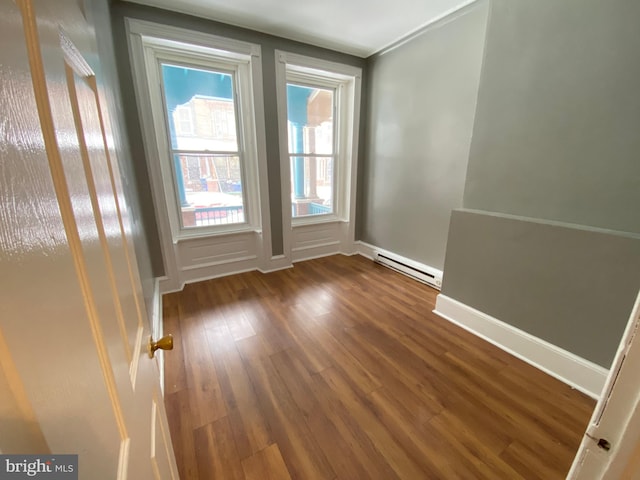 empty room with baseboard heating, plenty of natural light, dark wood-style floors, and baseboards