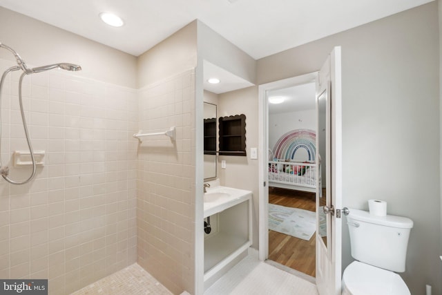 ensuite bathroom featuring tiled shower, toilet, and wood finished floors