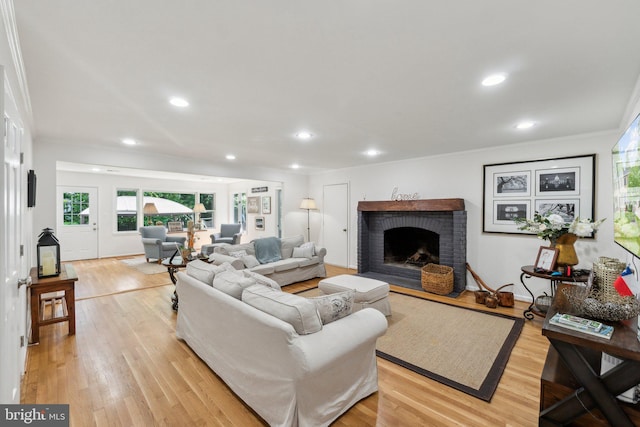 living room featuring a brick fireplace, light wood-type flooring, recessed lighting, and crown molding