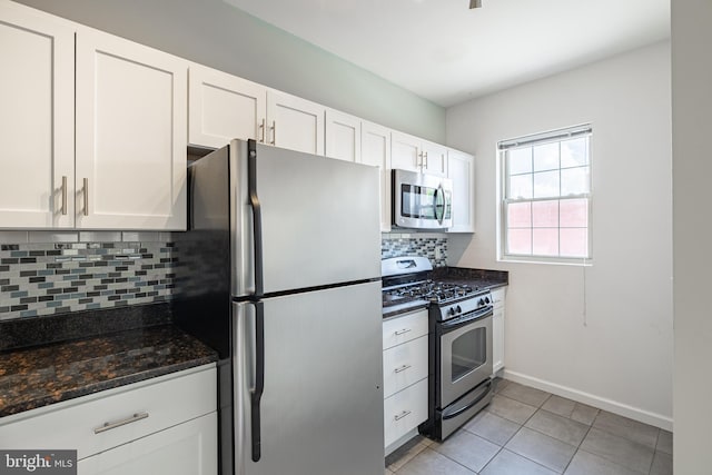 kitchen featuring appliances with stainless steel finishes, backsplash, white cabinetry, dark stone counters, and light tile patterned floors