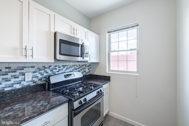 kitchen with stainless steel appliances, decorative backsplash, white cabinetry, and dark stone countertops