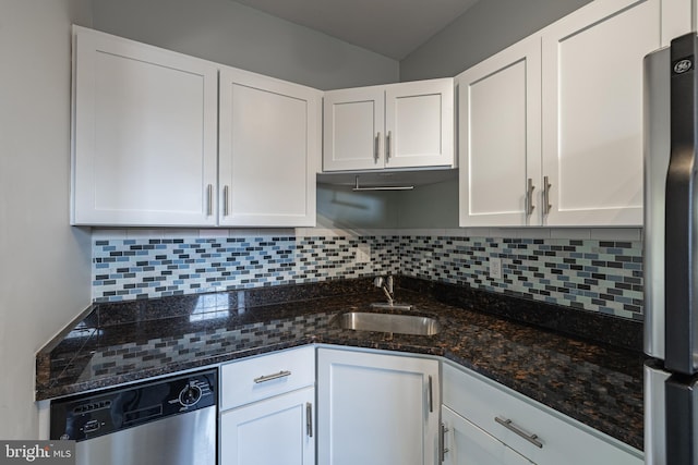 kitchen featuring appliances with stainless steel finishes, a sink, white cabinetry, dark stone counters, and backsplash