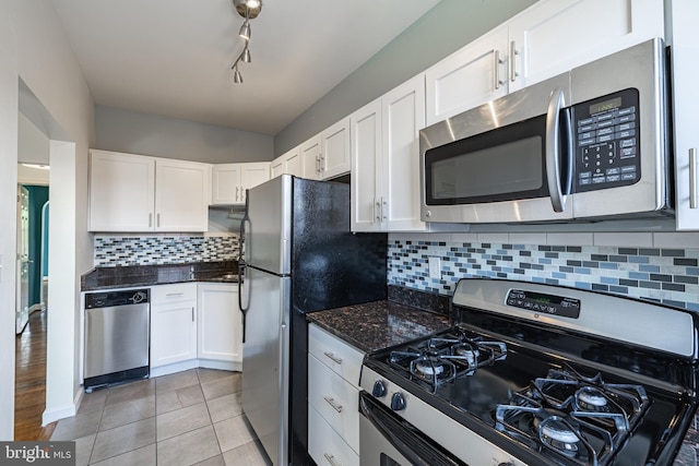 kitchen with stainless steel appliances, white cabinets, light tile patterned floors, and dark stone counters