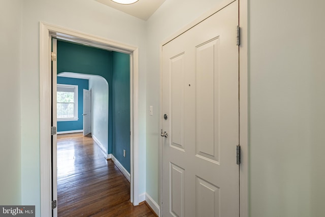 hall with dark wood finished floors, arched walkways, and baseboards