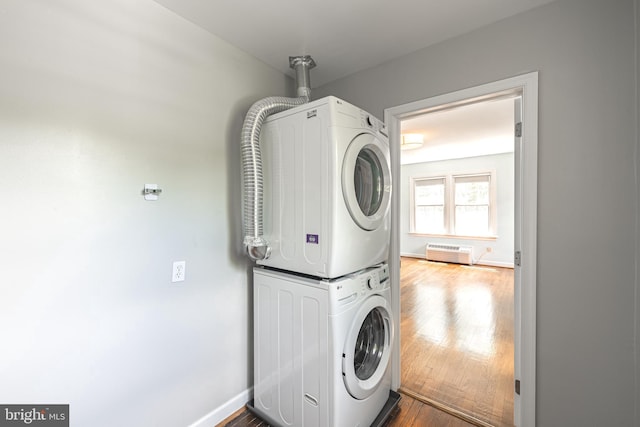 clothes washing area featuring stacked washer / dryer, dark wood-type flooring, and baseboards