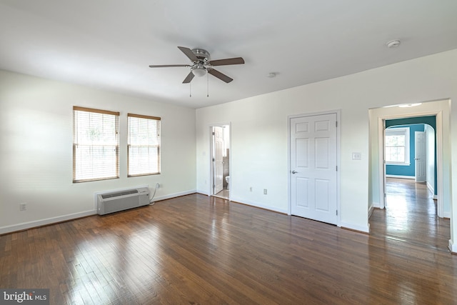 unfurnished bedroom featuring a wall mounted AC, dark wood finished floors, baseboards, arched walkways, and a ceiling fan