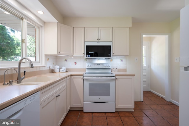 kitchen featuring white appliances, a sink, backsplash, white cabinetry, and tile patterned floors