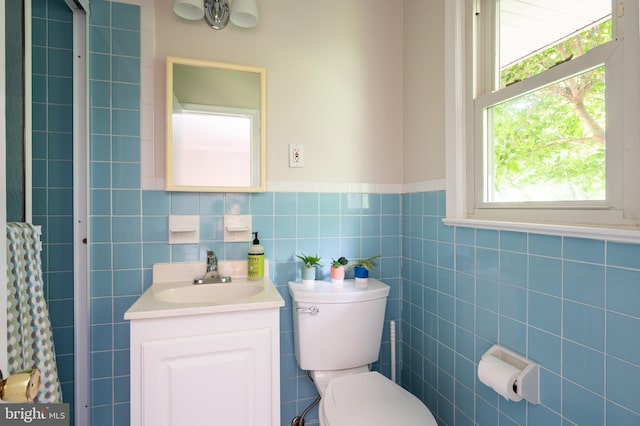 bathroom featuring vanity, toilet, tile walls, and a wainscoted wall