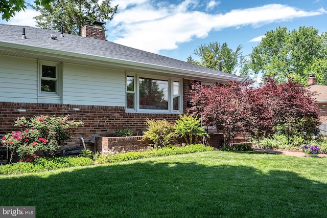 view of front facade with brick siding, a chimney, a front lawn, and roof with shingles
