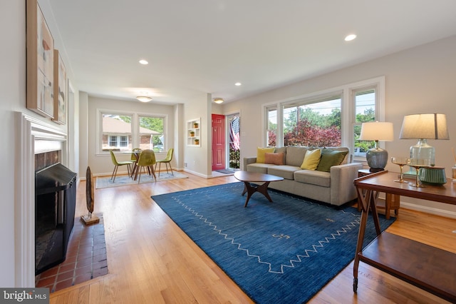 living area featuring a brick fireplace, light wood finished floors, baseboards, and recessed lighting