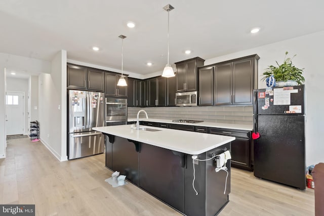 kitchen with appliances with stainless steel finishes, a sink, light countertops, tasteful backsplash, and light wood-type flooring