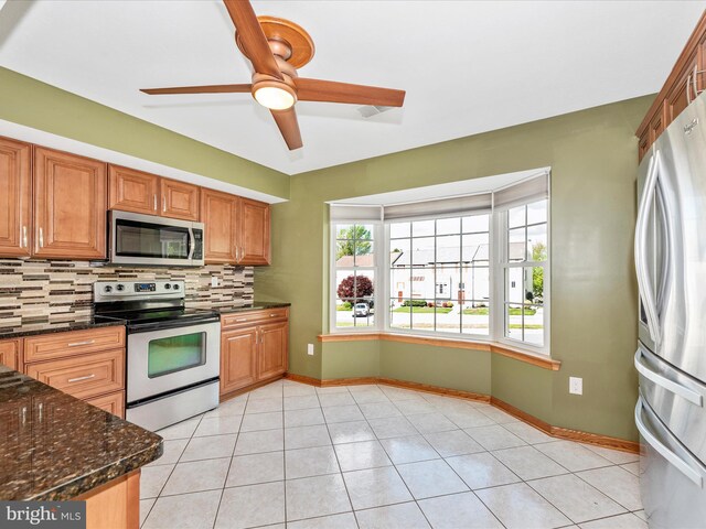 kitchen featuring stainless steel appliances, backsplash, a ceiling fan, baseboards, and dark stone countertops
