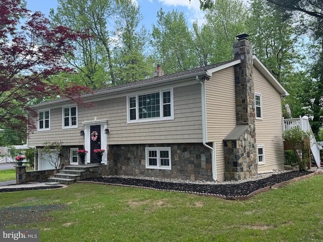 bi-level home featuring a chimney, a front yard, and stone siding