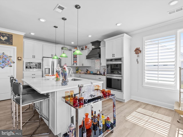 kitchen featuring stainless steel appliances, a sink, custom exhaust hood, light countertops, and a kitchen bar