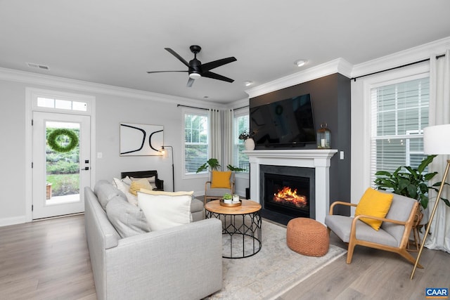 living room featuring wood finished floors, a fireplace with flush hearth, ornamental molding, a ceiling fan, and baseboards