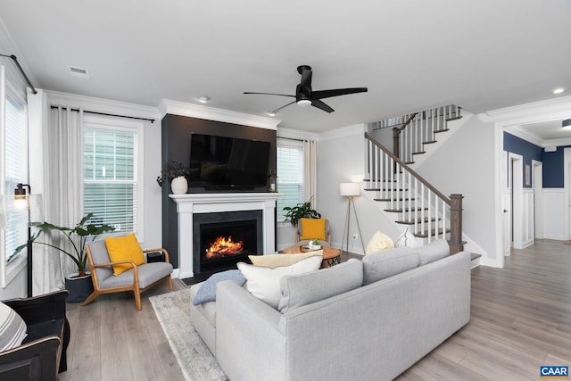 living room featuring crown molding, wood finished floors, stairs, a fireplace with flush hearth, and ceiling fan
