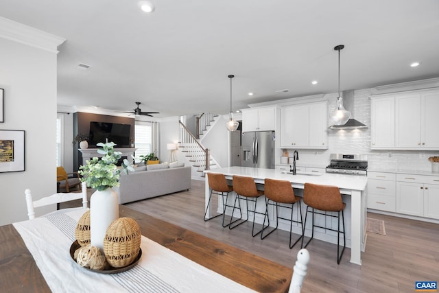 kitchen with appliances with stainless steel finishes, wall chimney range hood, a kitchen island with sink, a kitchen bar, and backsplash