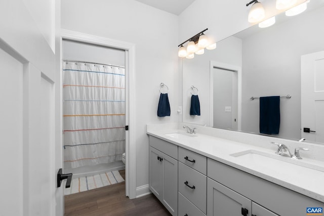 bathroom with wood finished floors, double vanity, toilet, and baseboards