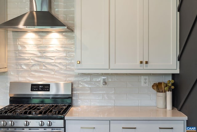 kitchen with stainless steel gas range, wall chimney exhaust hood, backsplash, white cabinets, and light stone countertops