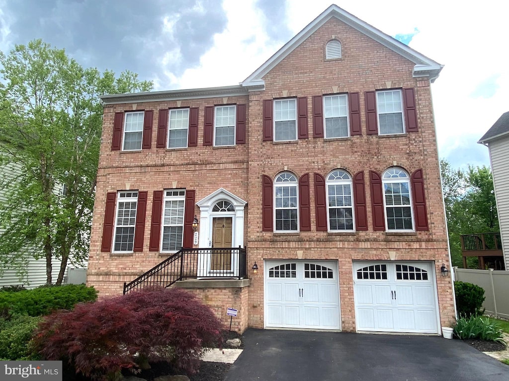 view of front of property featuring driveway, an attached garage, brick siding, and fence