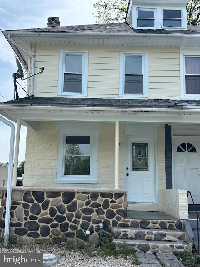 view of front of home with a porch, brick siding, and a chimney