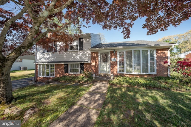 tri-level home with brick siding, central AC, and a front yard