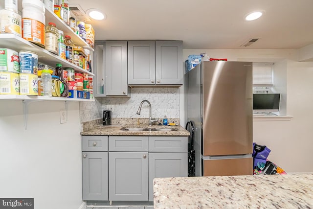 kitchen featuring freestanding refrigerator, a sink, gray cabinetry, decorative backsplash, and open shelves
