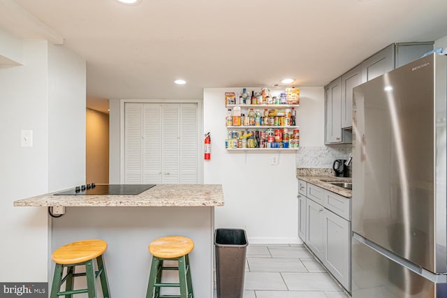 kitchen featuring freestanding refrigerator, a breakfast bar area, gray cabinets, recessed lighting, and decorative backsplash