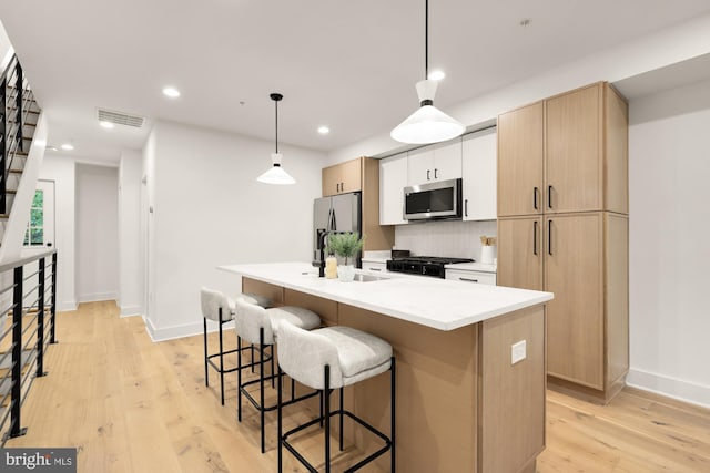 kitchen featuring appliances with stainless steel finishes, a breakfast bar, a center island with sink, light wood-style flooring, and backsplash