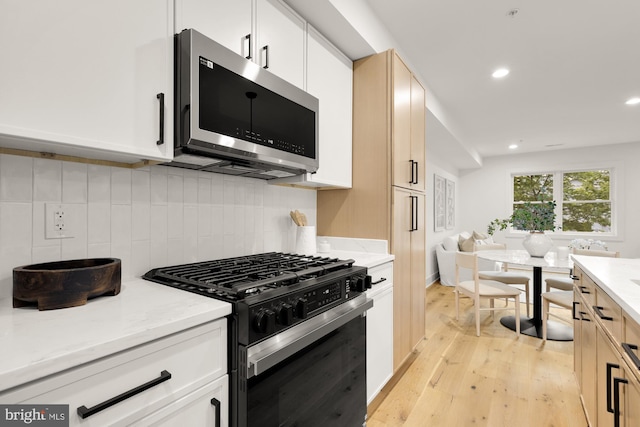 kitchen with stainless steel microwave, black range with gas stovetop, light wood-style flooring, light stone counters, and recessed lighting