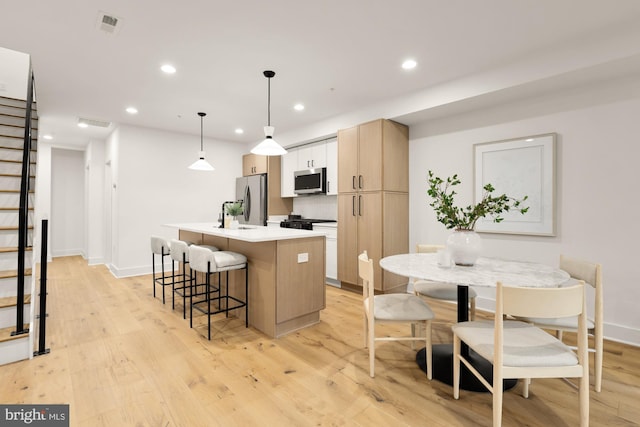 kitchen with stainless steel appliances, recessed lighting, a center island with sink, light wood-style floors, and baseboards