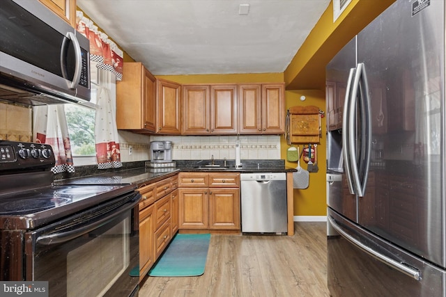 kitchen featuring stainless steel appliances, light wood-type flooring, a sink, brown cabinetry, and tasteful backsplash