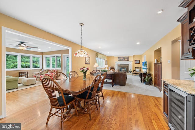 dining room featuring beverage cooler, light wood-style floors, a glass covered fireplace, ceiling fan, and recessed lighting
