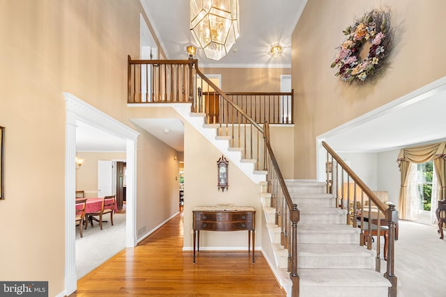stairway featuring a towering ceiling, a chandelier, wood finished floors, and baseboards