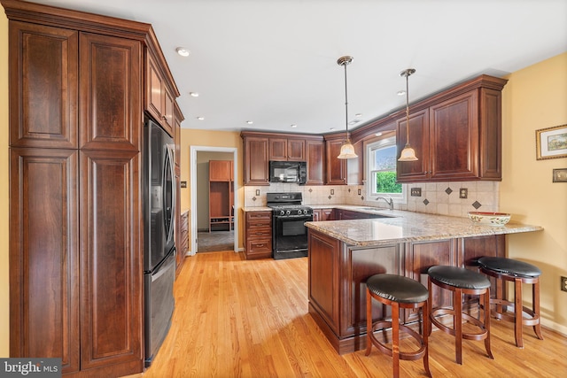 kitchen with black appliances, a sink, a peninsula, light wood-style floors, and tasteful backsplash