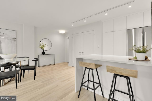 kitchen with freestanding refrigerator, a breakfast bar area, white cabinets, light wood-style floors, and rail lighting