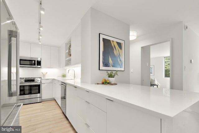 kitchen with stainless steel appliances, a sink, a peninsula, track lighting, and white cabinets