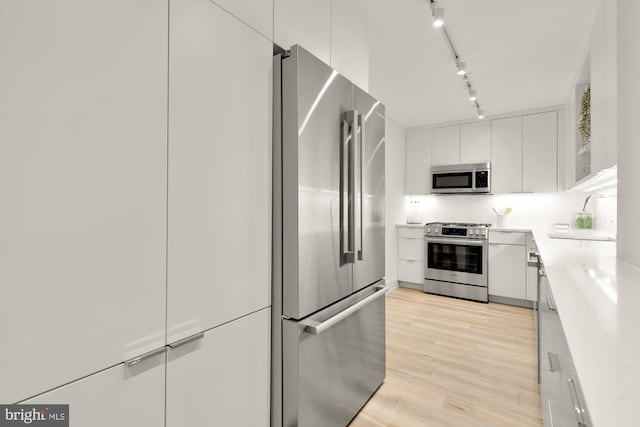 kitchen featuring appliances with stainless steel finishes, a sink, rail lighting, light countertops, and white cabinetry