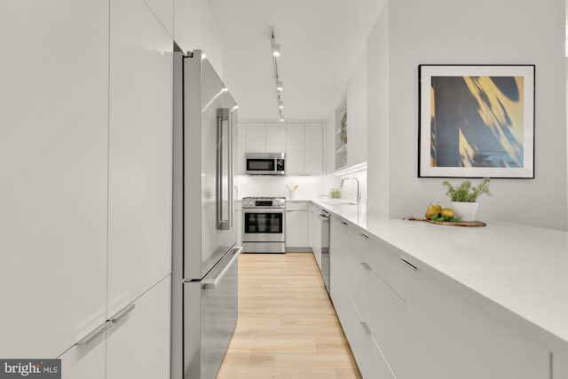 kitchen with stainless steel appliances, white cabinets, light wood-type flooring, light countertops, and modern cabinets