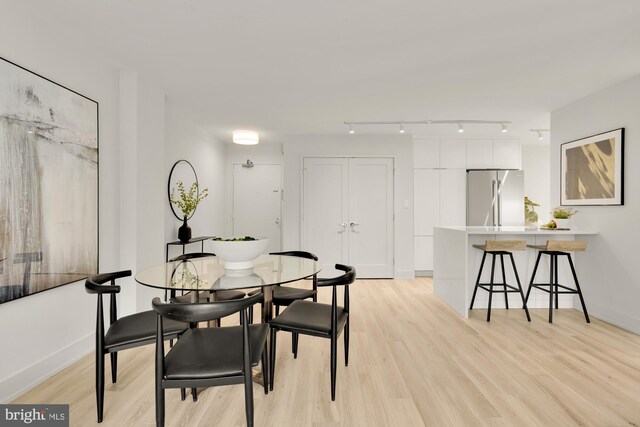 dining area featuring light wood-style flooring, rail lighting, and baseboards