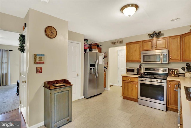 kitchen with stainless steel appliances, brown cabinets, light countertops, and baseboards