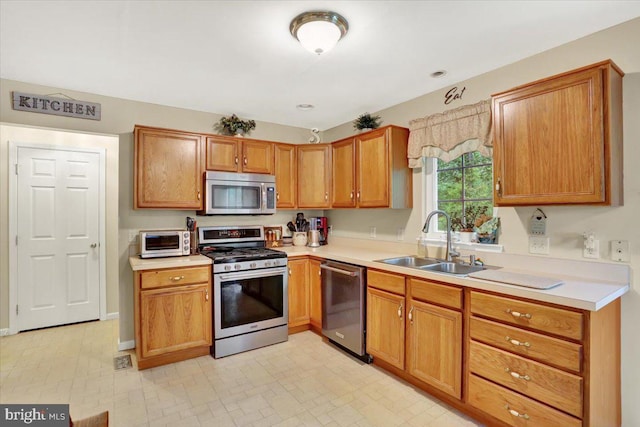 kitchen with appliances with stainless steel finishes, a sink, light countertops, and brown cabinetry
