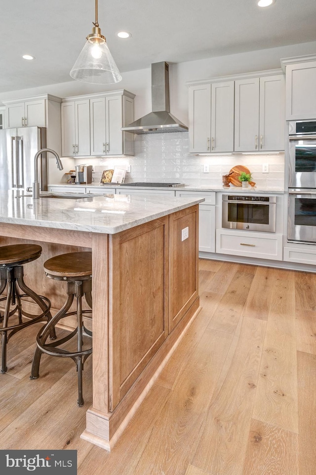 101 Eagle Dr, Broomall, PA 19008 - kitchen featuring wall chimney range hood, stainless steel appliances, a sink, light wood-style flooring, and a kitchen breakfast bar