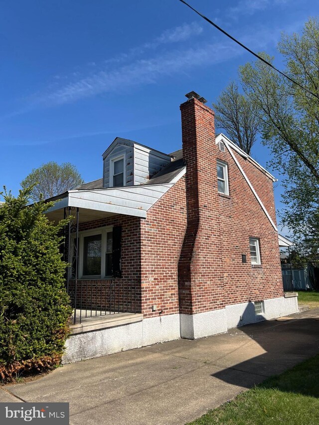view of property exterior with a chimney, brick siding, and a porch